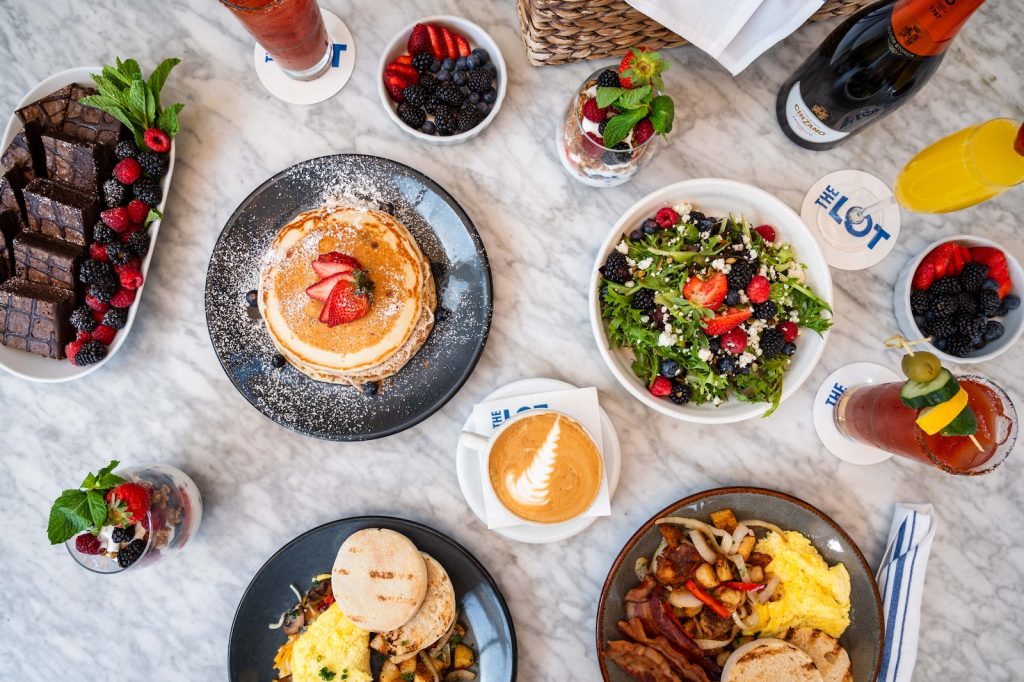 Brunch foods at THE LOT in La Jolla, including pancakes, an omelette, scrammbled eggs, salad, mimosas, a bloody Mary, a late, and more.